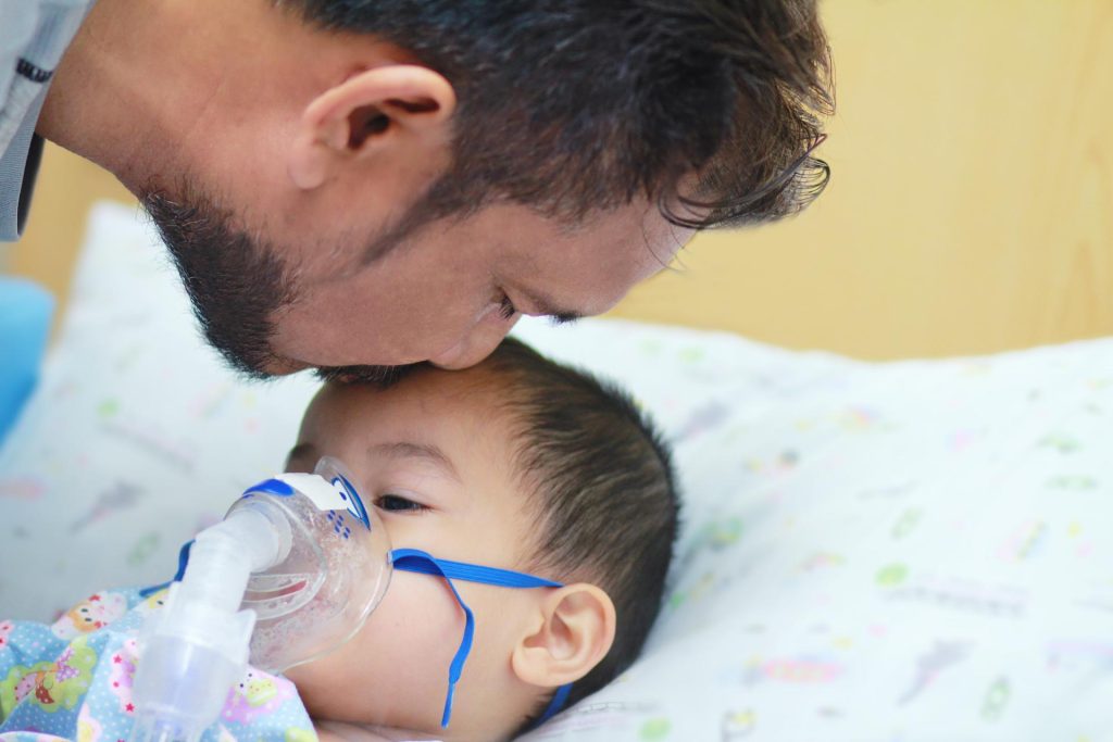 Hombre da un beso en la frente a un niño con máscara de oxígeno